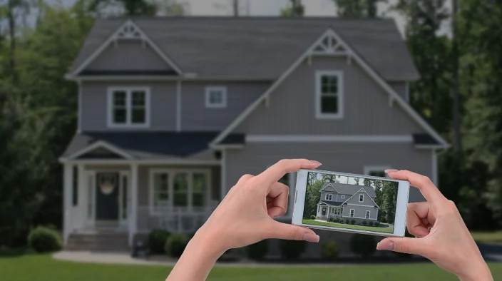 womans hands holding phone and taking picture of house